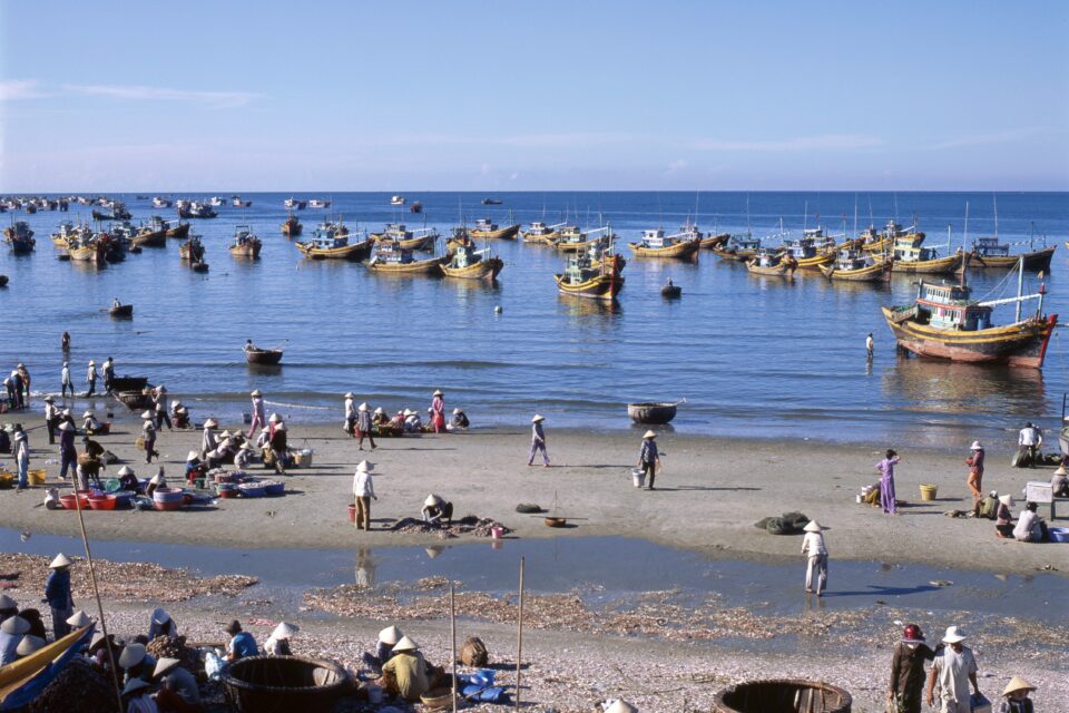 Urokliwa rybacka wioska z kolorowymi łodziami i mieszkańcami pracującymi na plaży.